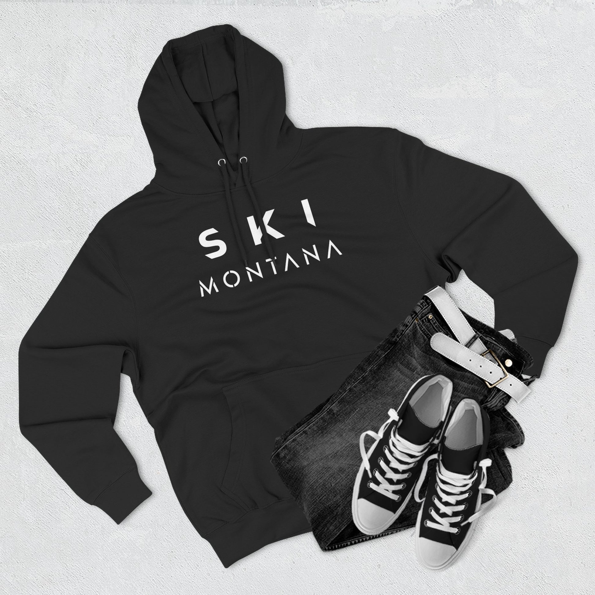 Black hoodie with 'Ski Montana' text, black jeans, and black sneakers on a light gray background