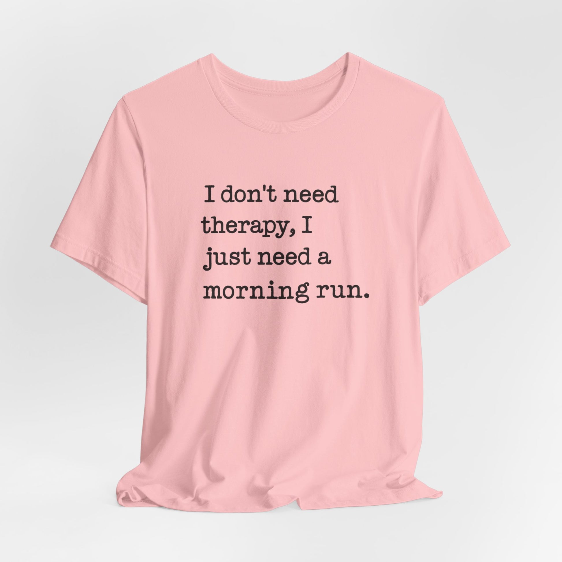 Pink t-shirt with text 'I don't need therapy, I just need a morning run.' on a light gray background
